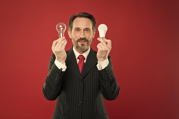 Photo man bearded consultant formal suit hold light bulb on red background symbol of idea progress and innovation environment friendly lighting energy efficient lighting lighting choices to save money