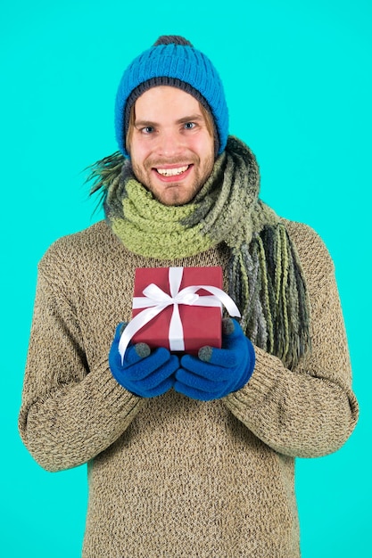 Man bearded handsome wear winter hat scarf gloves hold gift box. Hipster hold christmas gift with bow. Holiday present concept. Winter holidays. Give gift spread happiness. Ready to make her happy.