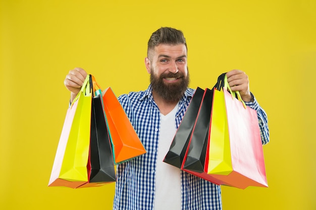 Мужчина бородатый хипстер с веселым лицом носит бумажные пакеты для покупок на желтом фоне