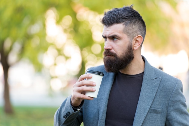 Man bearded hipster prefer coffee take away Businessman drink coffee outdoors Reloading energy Relaxing coffee break Hipster hold paper coffee cup and enjoy nature environment Drink it on the go