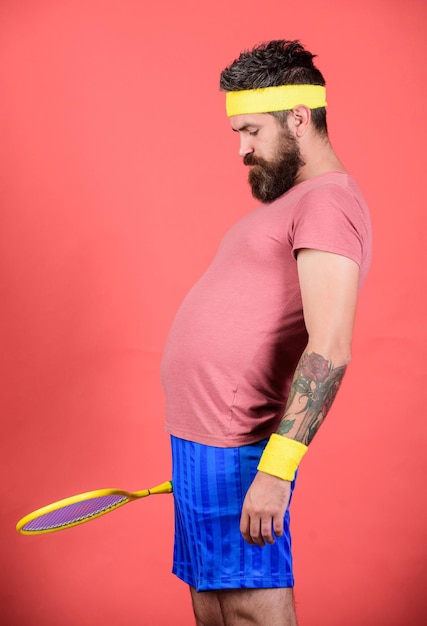 Man bearded hipster wear old school sport outfit with bandages. Athlete hold tennis racket in hand on red background. Tennis can be an effective way to lose weight. Tennis club concept. Tennis sport.