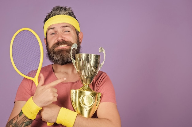 Photo man bearded successful athlete first place sport achievement tennis champion win tennis game celebrate victory athletic man hold tennis racket and golden goblet tennis player win championship