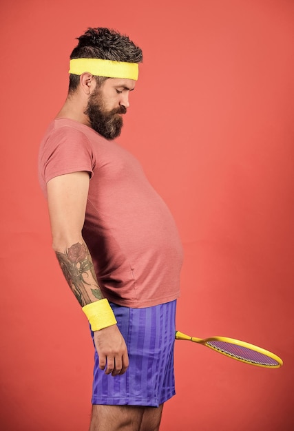 Man bebaarde hipster draagt old school sportoutfit met verband Atleet houdt tennisracket in de hand op rode achtergrond Tennis kan een effectieve manier zijn om gewicht te verliezen Tennisclub concept Tennissport