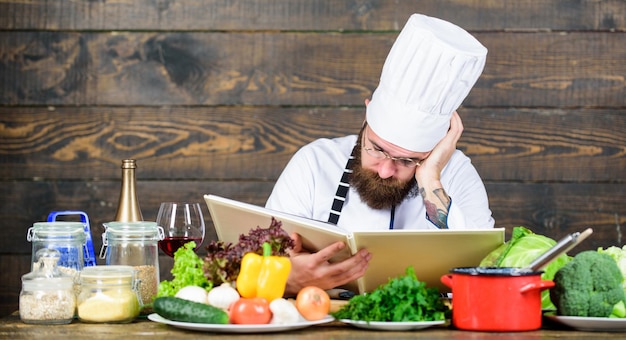 Man bebaarde hipster lees boek recept in de buurt van tafel verse groenten Culinaire kunsten Recept om gezond voedsel te koken Ervaren chef-kok kookt uitstekend gerecht Dit recept is gewoon perfect Vegetarisch recept