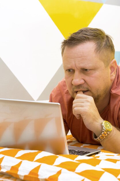 Foto uomo sul letto che lavora su un computer portatile. emozioni umane