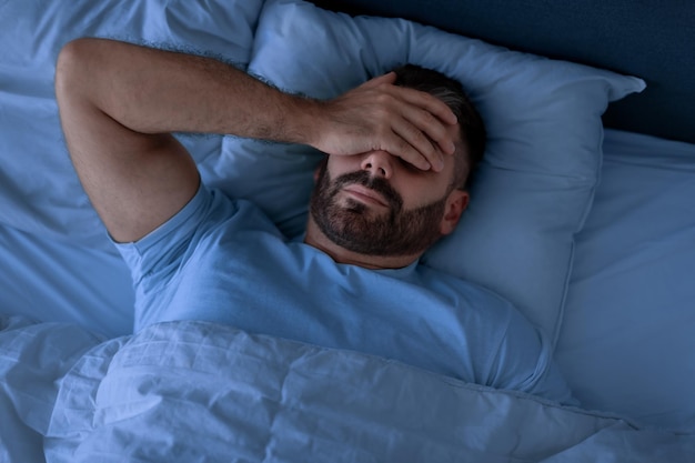 Foto man bedekt zijn gezicht met zijn hand en ligt niet te slapen in de slaapkamer.