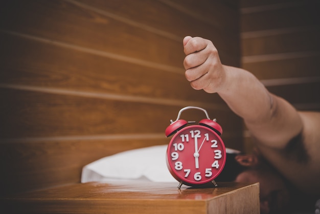 Photo man being awakened by an alarm clock in his bedroom.