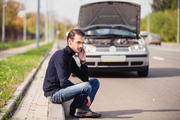 Man belt via de telefoon om hulp te krijgen met zijn beschadigde auto