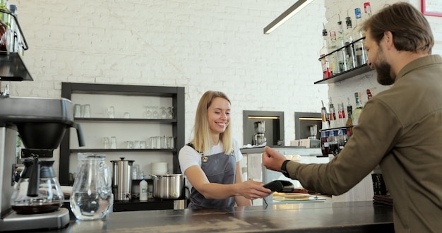 Man betaalt voor afhaalkoffie met nfc-technologie door smartwatch contactloos op terminal in modern café. Niet-contant betalingsconcept.