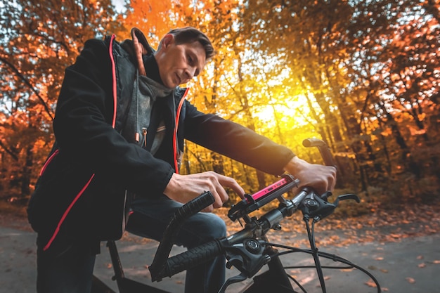 A man on a bicycle uses a phone on the steering wheel in an autumn forest in the evening at sunset