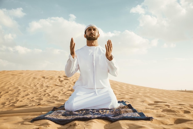 Man bidt op het zand in de woestijn tegen de lucht