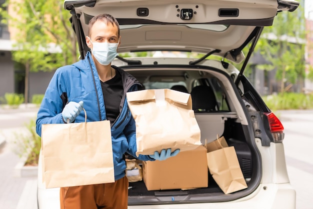 Man bij de auto. Kerel in een bezorguniform. Man met een medisch masker. Coronavirus-concept.