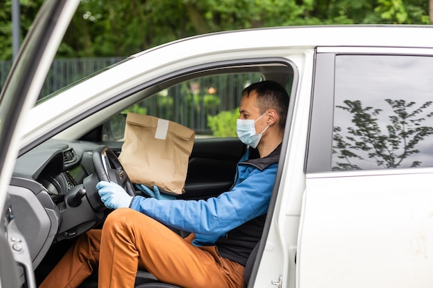 Man bij de auto. Kerel in een bezorguniform. Man met een medisch masker. Coronavirus-concept.