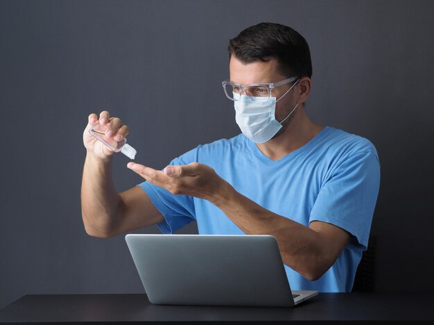 Man bij quarantine coronavirus met beschermend masker werkt online met laptop. handen wassen met alcoholgel ontsmettingsmiddel om handen te reinigen.