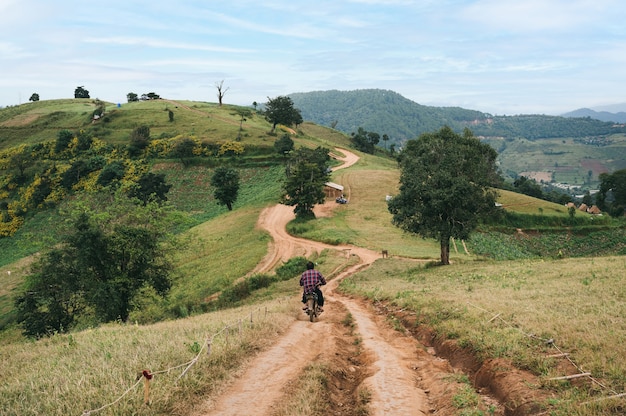 Photo man biking old motorcycle on gravel road down to green hill at countryside