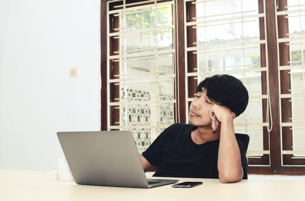 The man in black Asian t-shirt sat in front of the laptop with a sad expression