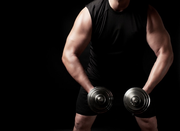 Man in black clothes holds steel dumbbells in his hands, his muscles are tense