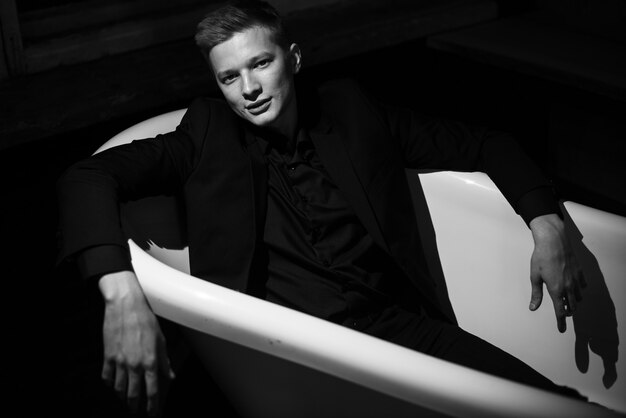 Photo man in black clothes is lying in empty bath