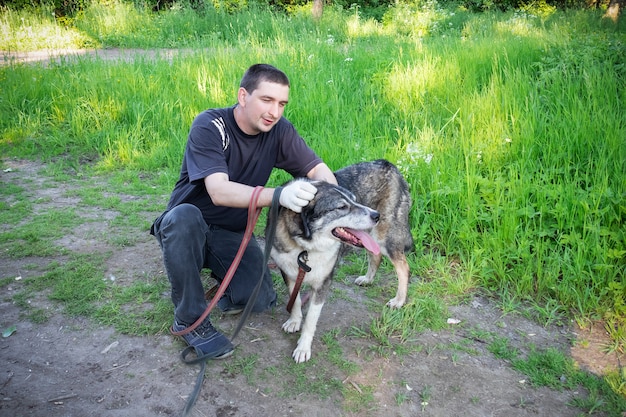 Uomo in abiti neri con cane grigio seduto tra l'erba verde.