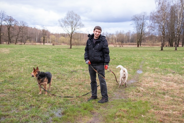 Man in black clothes with two dogson on leashes standing on green grass field