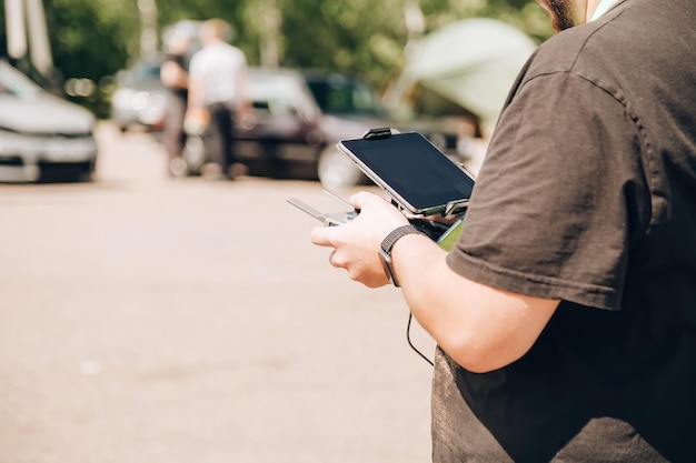 Un uomo in nero controlla un drone utilizzando un telecomando e un tablet è in piedi in un parcheggio