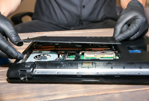 Man in black gloves is repairing a laptop. Service center worker is fixing problems.