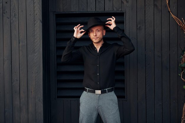 Photo man in black hat standing against black wooden building exterior