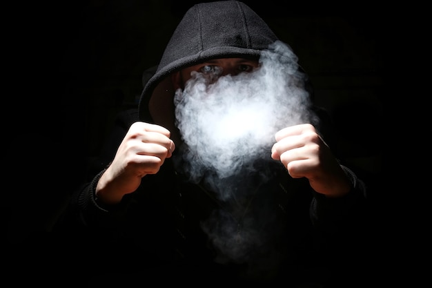 Man in a black hood and smoke on a black background