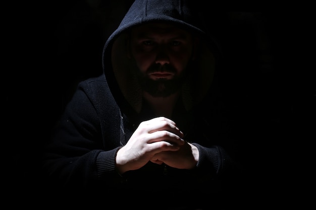 Man in a black hood and smoke on a black background