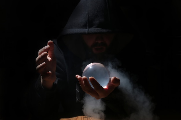 Man in a black hood with cristal ball summon evil