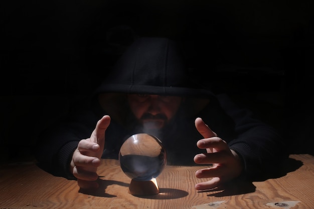 Man in a black hood with cristal ball summon evil