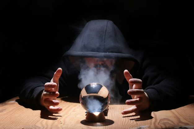 Man in a black hood with cristal ball summon evil