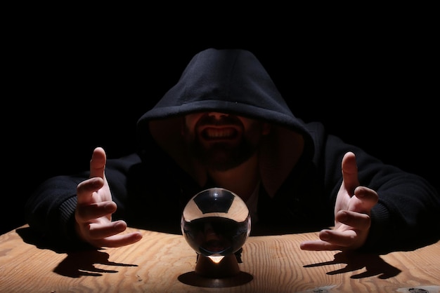 Man in a black hood with cristal ball summon evil