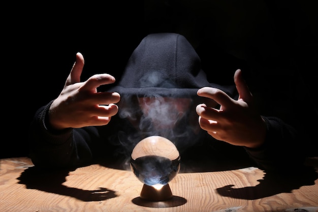 Man in a black hood with cristal ball summon evil