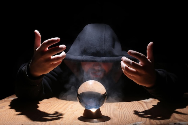 Man in a black hood with cristal ball summon evil