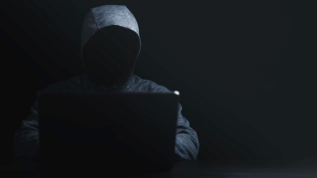 Man in black hoodie using computer laptop to unlock password for hacker in computer security system and financial technology malware concept