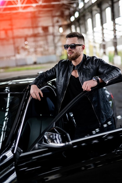 Man in black jacket standing near opened car door. Fashionable portrairt of car and driver.