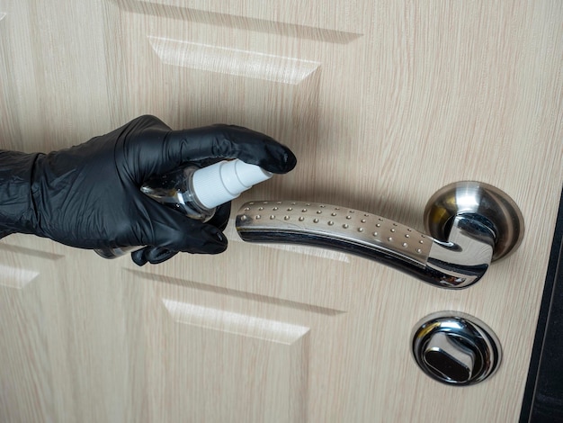 A man in black latex gloves sprays antiseptic on the door handle. Processing items to reduce the chance of infection with viruses