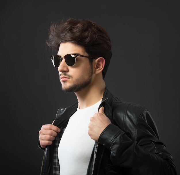 Man in black leather jacket looking over his sunglasses studio shot dark background