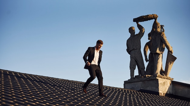 Man in black luxury clothes walk on the rooftop near the statue.