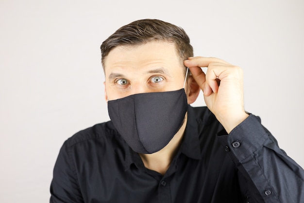 A man in a black medical mask looks at the camera on a white background