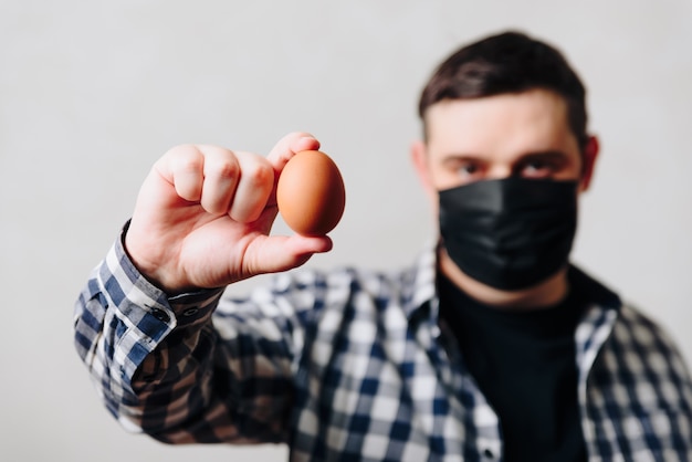 Foto un uomo con una maschera medica nera con un uovo di gallina in mano