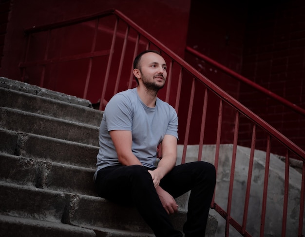 A man in black pants and a gray-blue T-shirt sits on the steps and smiles