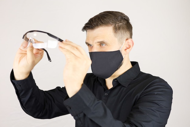 A man in a black protective mask looks into medical glasses on a white background