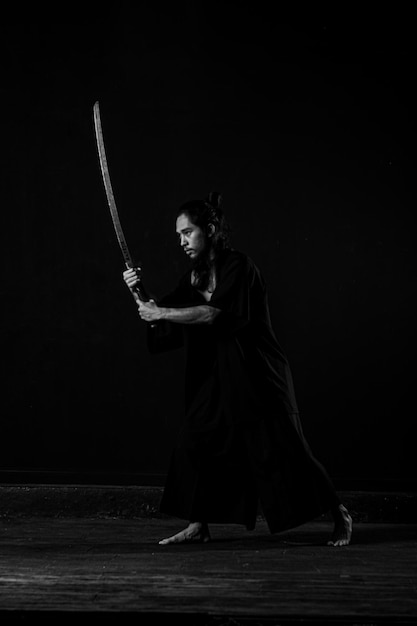 A man in a black robe holds a sword in his hands.