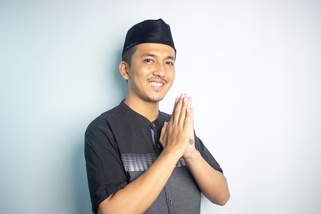 A man in a black shirt is standing in a white room and is wearing a black shirt and a black hat.