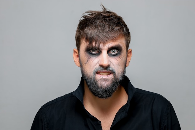 A man in a black shirt stands on a white background who has undead-style makeup for Halloween