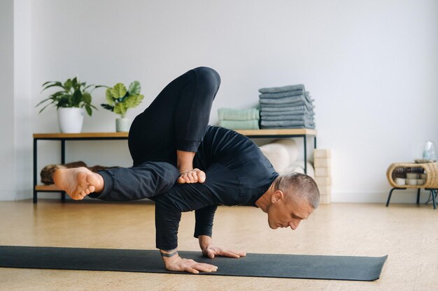 A man in black sportswear does yoga standing on his hands stretching in the gym