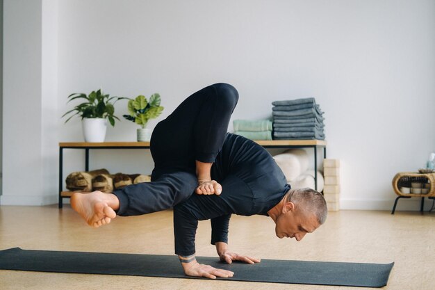 A man in black sportswear does yoga standing on his hands stretching in the gym