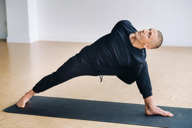 a man in black sportswear is doing yoga stretching in the gym